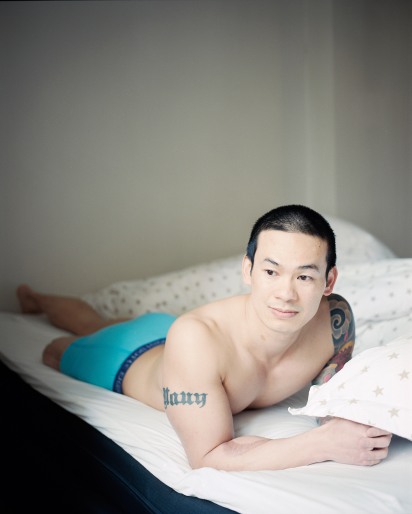 En ung mann i 20-årene med asiatisk utseende ligger på magen i en seng. Dyna ligger ved siden av ham. Mannen har kort, sort hår, brune øyne og en muskuløs overkropp. Han hviler på albuene, og har kun en turkis boksershorts på seg. På sin høyre overarm har han tatovert «Nauy». På den andre skuldra har han en stor, detaljert, fargerik tatovering. Hans høyrefot er amputert ved låret. Mannen har blikket vendt til siden og har et lett smil.